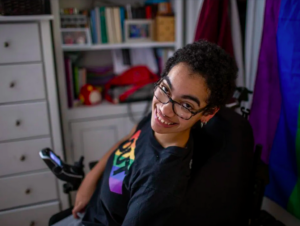 LGBT person in rainbow shirt with glasses sitting in wheelchair