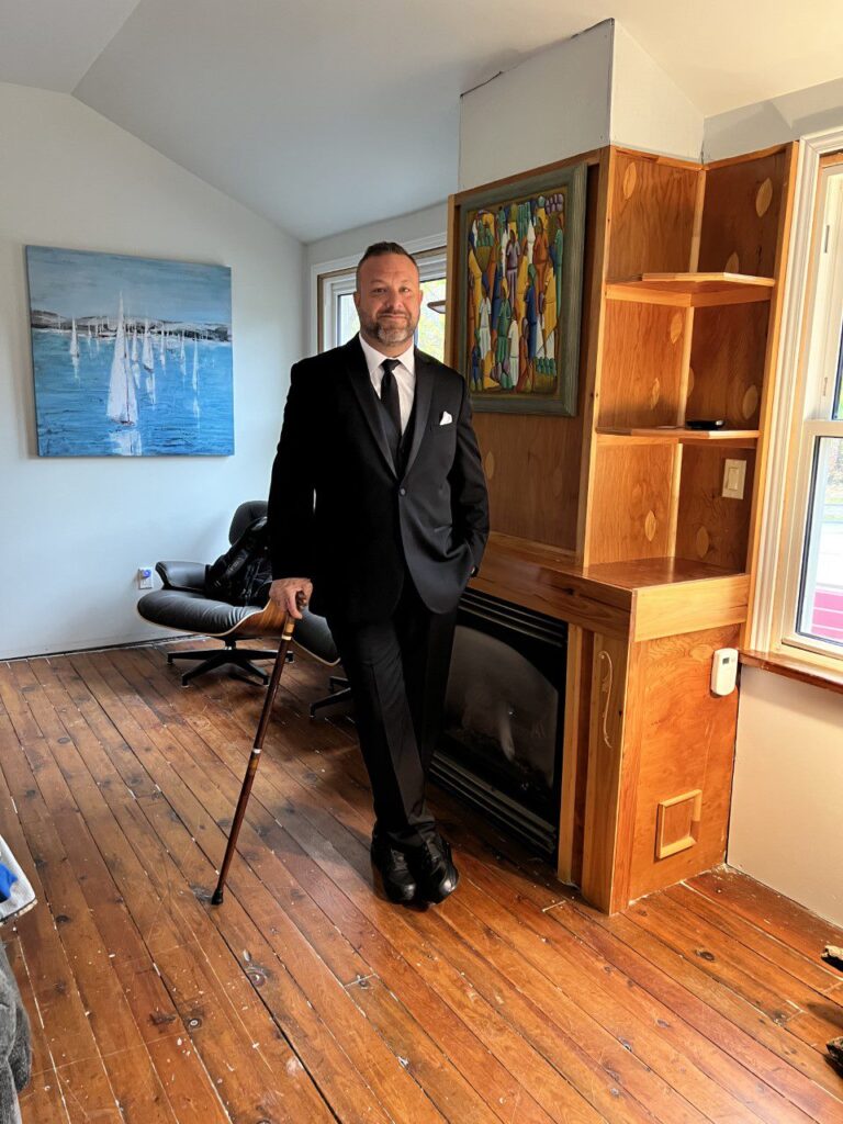 Middle aged man in suit, standing in living room with a cane.