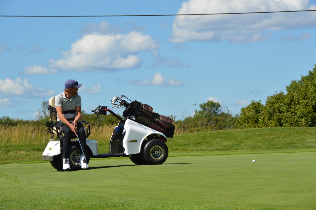 man sitting in an adaptive golf cart teeing up a shot