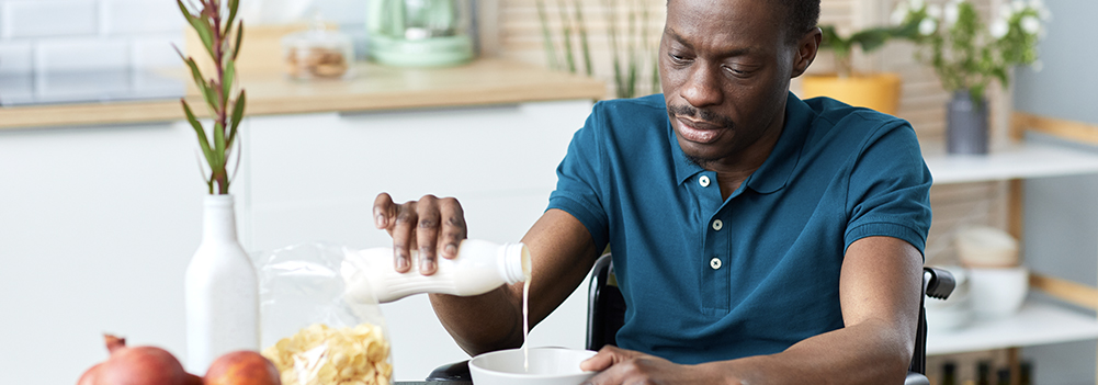 Man who uses a wheelchair pouring milk on healthy cereal
