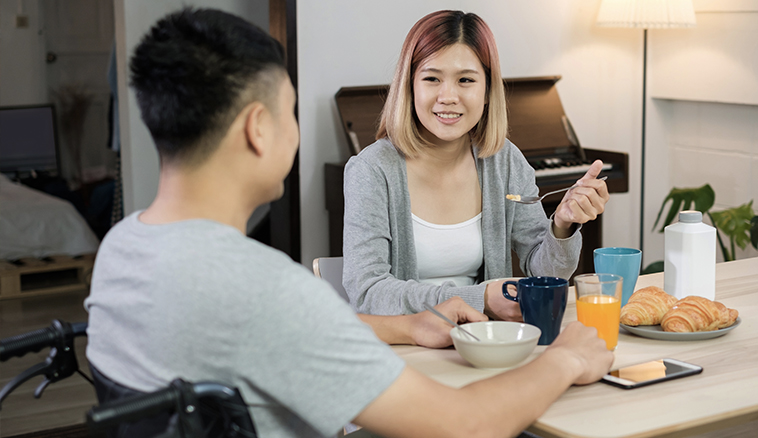 Young asian man in a wheelchair having breakfast with his female friend.