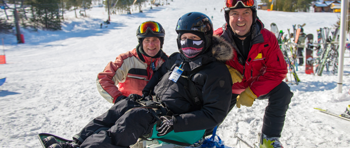 A sit-skier with his two friends pose on the mountain.