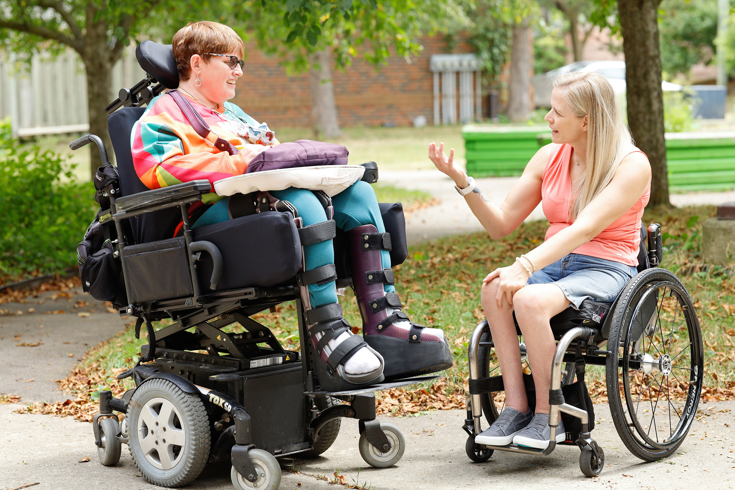 two women in wheelchairs having a chat outdoors